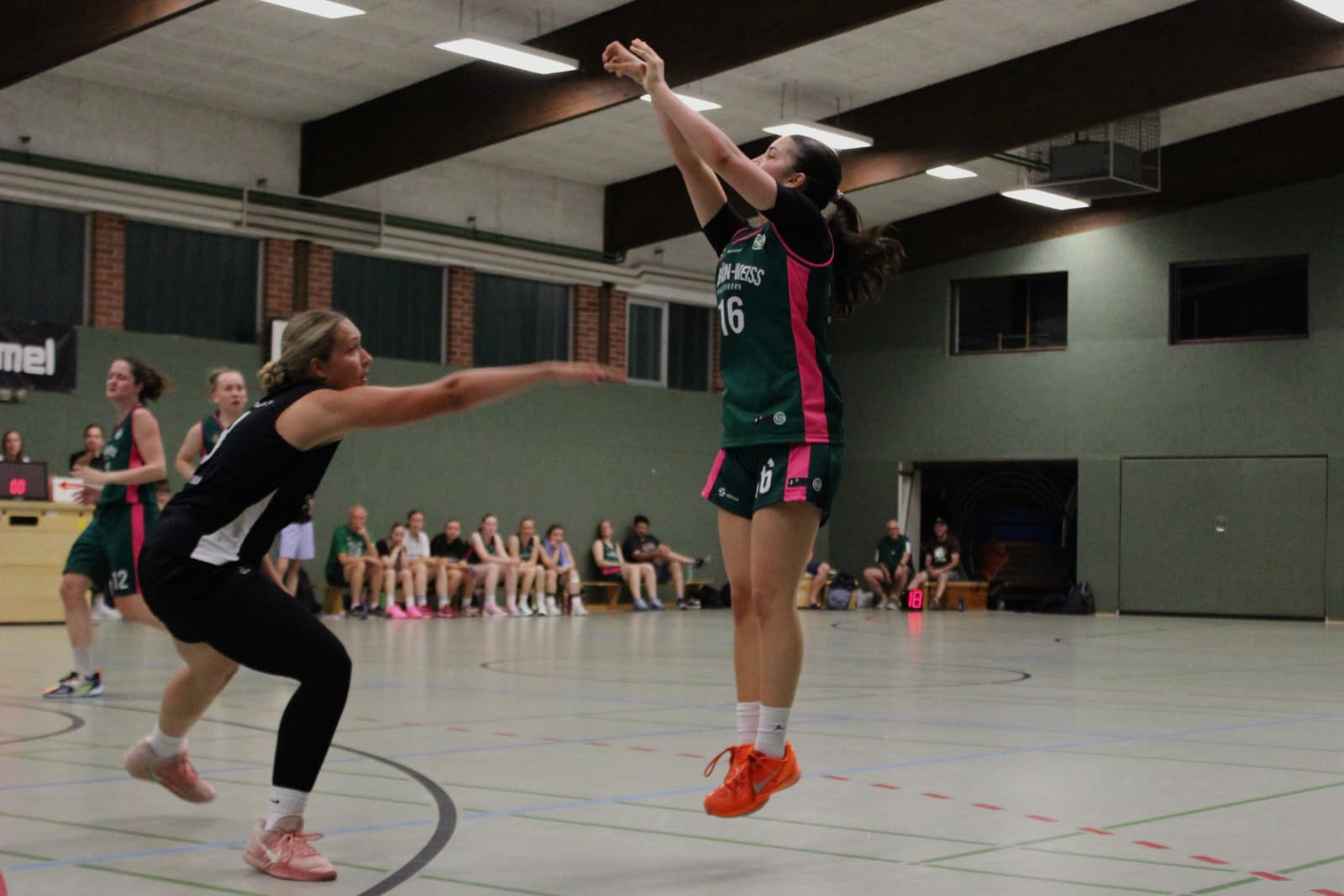 Spielerin im grünen Trikot wirft aus dem Sprung auf den Korb