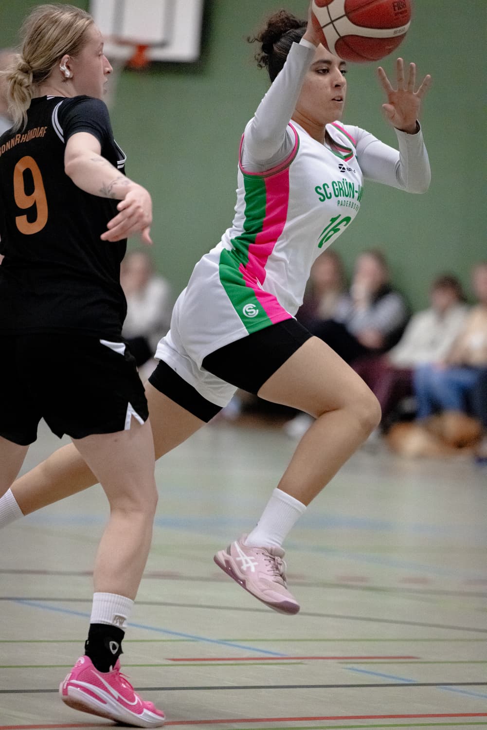 Spielerin im weiß-grünen Trikot springt mit dem Ball an einer Gegnerin vorbei
